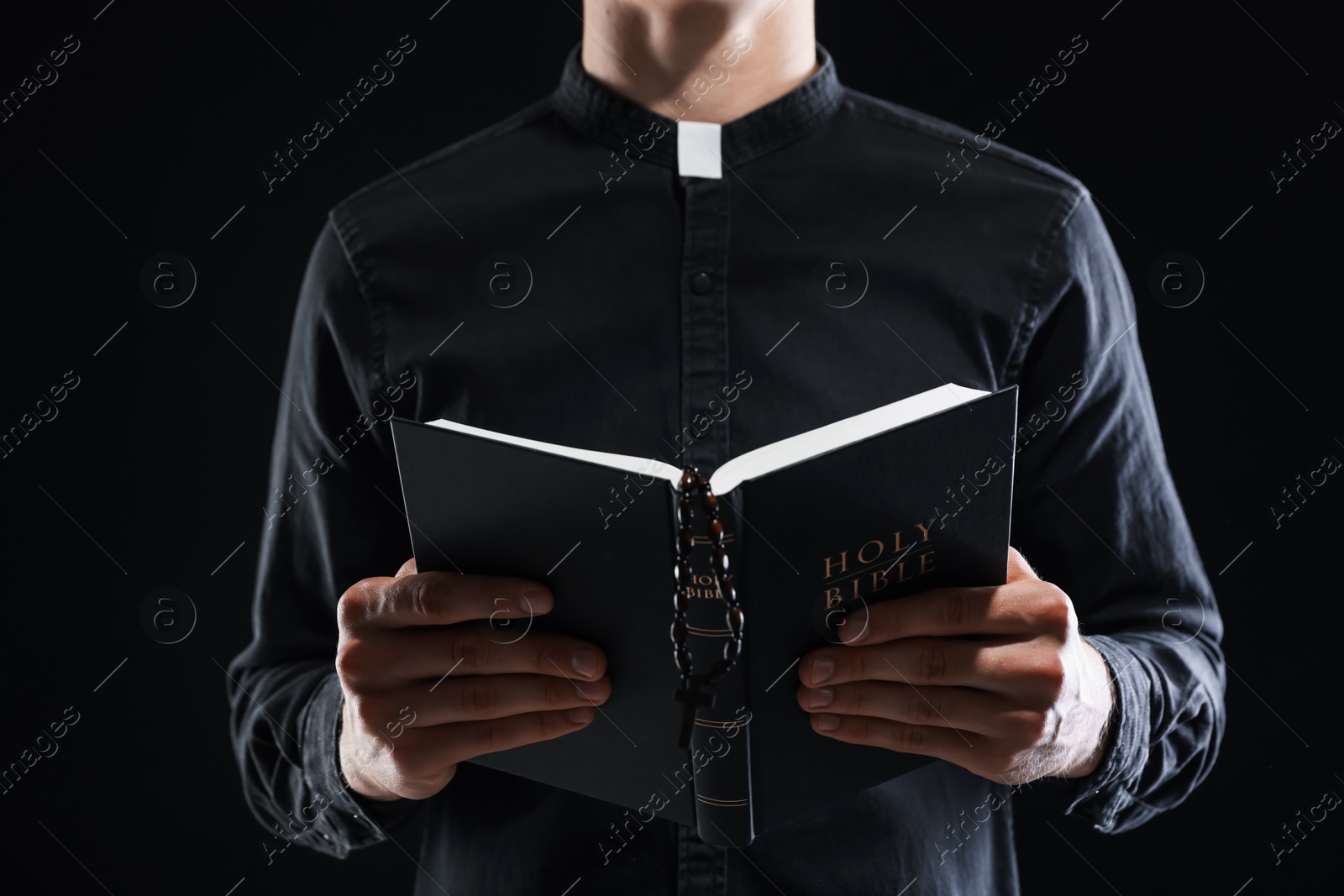 Photo of Priest with Holy Bible on black background, closeup