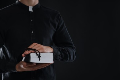 Photo of Priest with rosary and Holy Bible on black background, closeup. Space for text