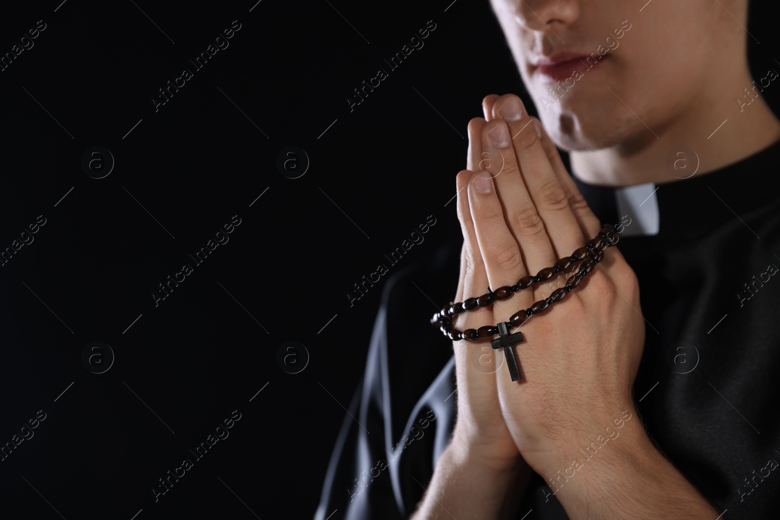 Photo of Priest with rosary praying on dark background, closeup. Space for text