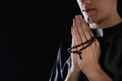 Photo of Priest with rosary praying on dark background, closeup. Space for text