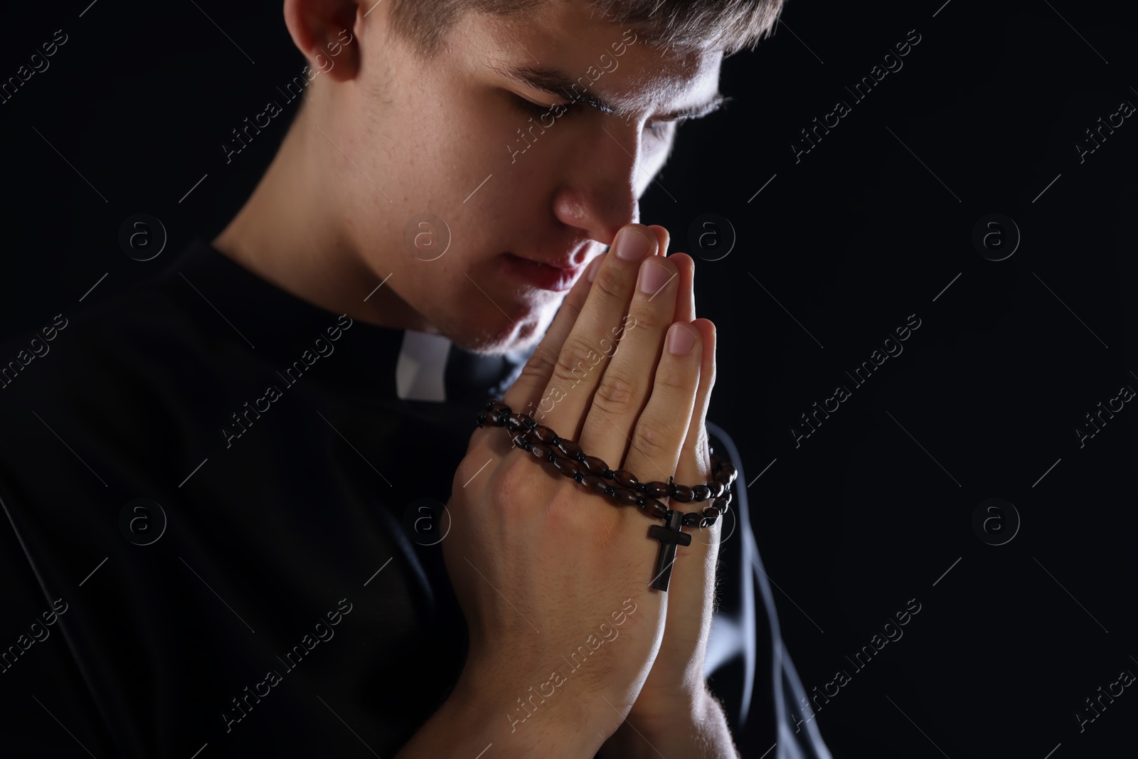 Photo of Priest with rosary praying on black background, space for text