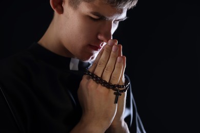 Photo of Priest with rosary praying on black background, space for text