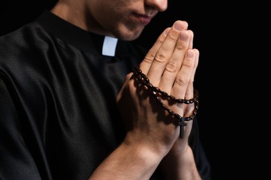 Photo of Priest with rosary praying on black background, closeup