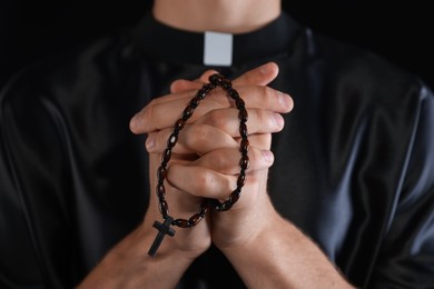 Photo of Priest with rosary praying on black background, closeup