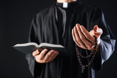 Photo of Priest with Holy Bible and rosary preaching on black background, closeup