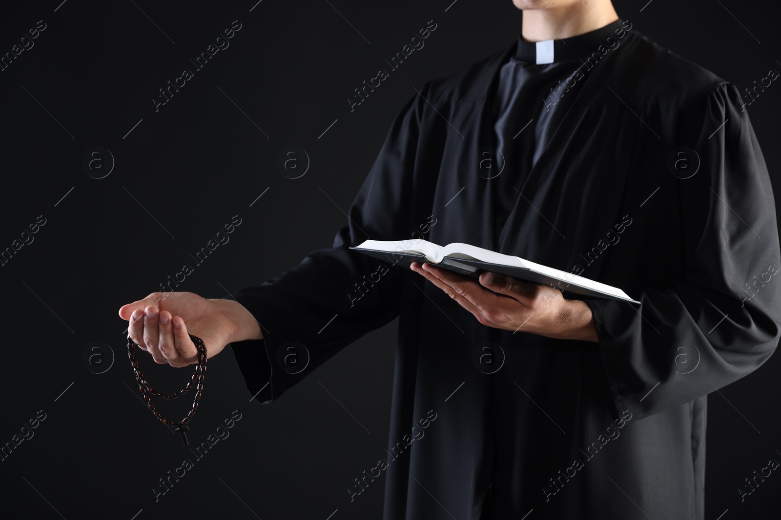 Photo of Priest with Holy Bible and rosary preaching on black background, closeup