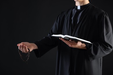 Photo of Priest with Holy Bible and rosary preaching on black background, closeup