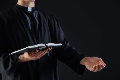 Photo of Priest with Holy Bible and rosary preaching on black background, closeup