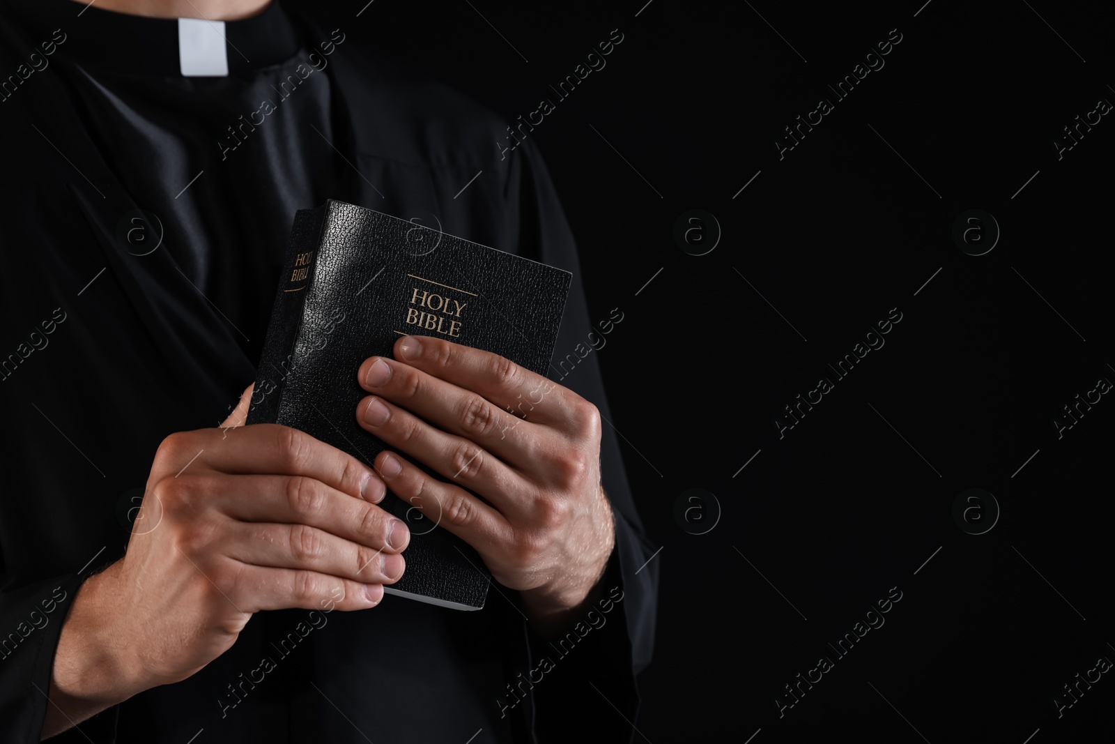 Photo of Priest with Holy Bible on black background, closeup. Space for text