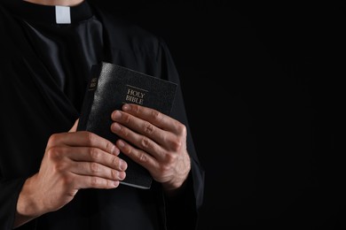 Photo of Priest with Holy Bible on black background, closeup. Space for text