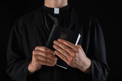 Photo of Priest with Holy Bible on black background, closeup