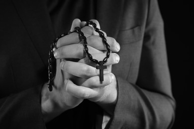 Photo of Priest with rosary praying on dark background, closeup. Black and white effect