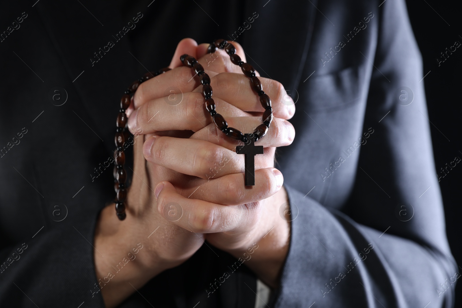 Photo of Priest with rosary praying on black background, closeup
