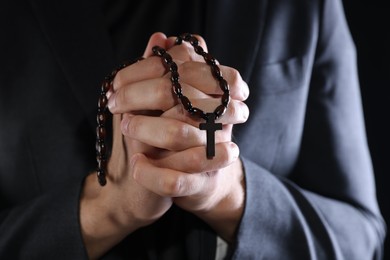 Photo of Priest with rosary praying on black background, closeup