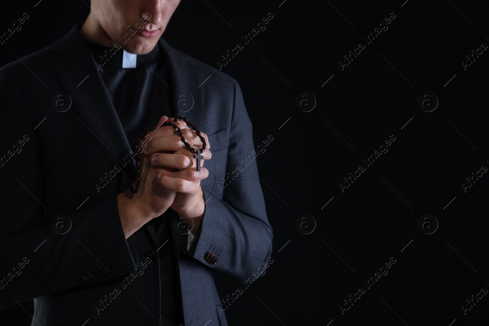 Photo of Priest with rosary praying on black background, closeup. Space for text
