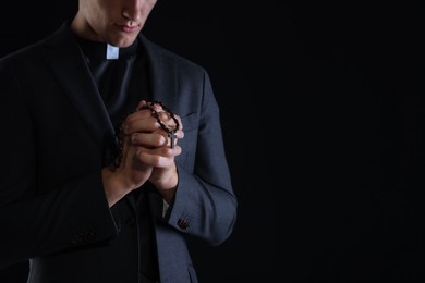 Photo of Priest with rosary praying on black background, closeup. Space for text