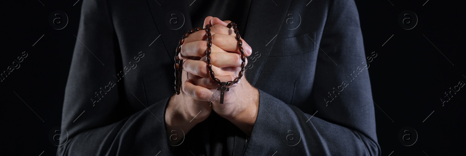 Photo of Priest with rosary praying on black background, closeup