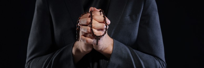 Photo of Priest with rosary praying on black background, closeup