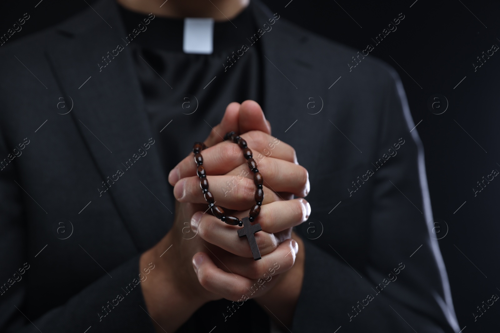 Photo of Priest with rosary praying on black background, closeup