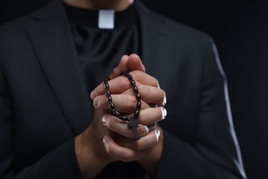 Photo of Priest with rosary praying on black background, closeup