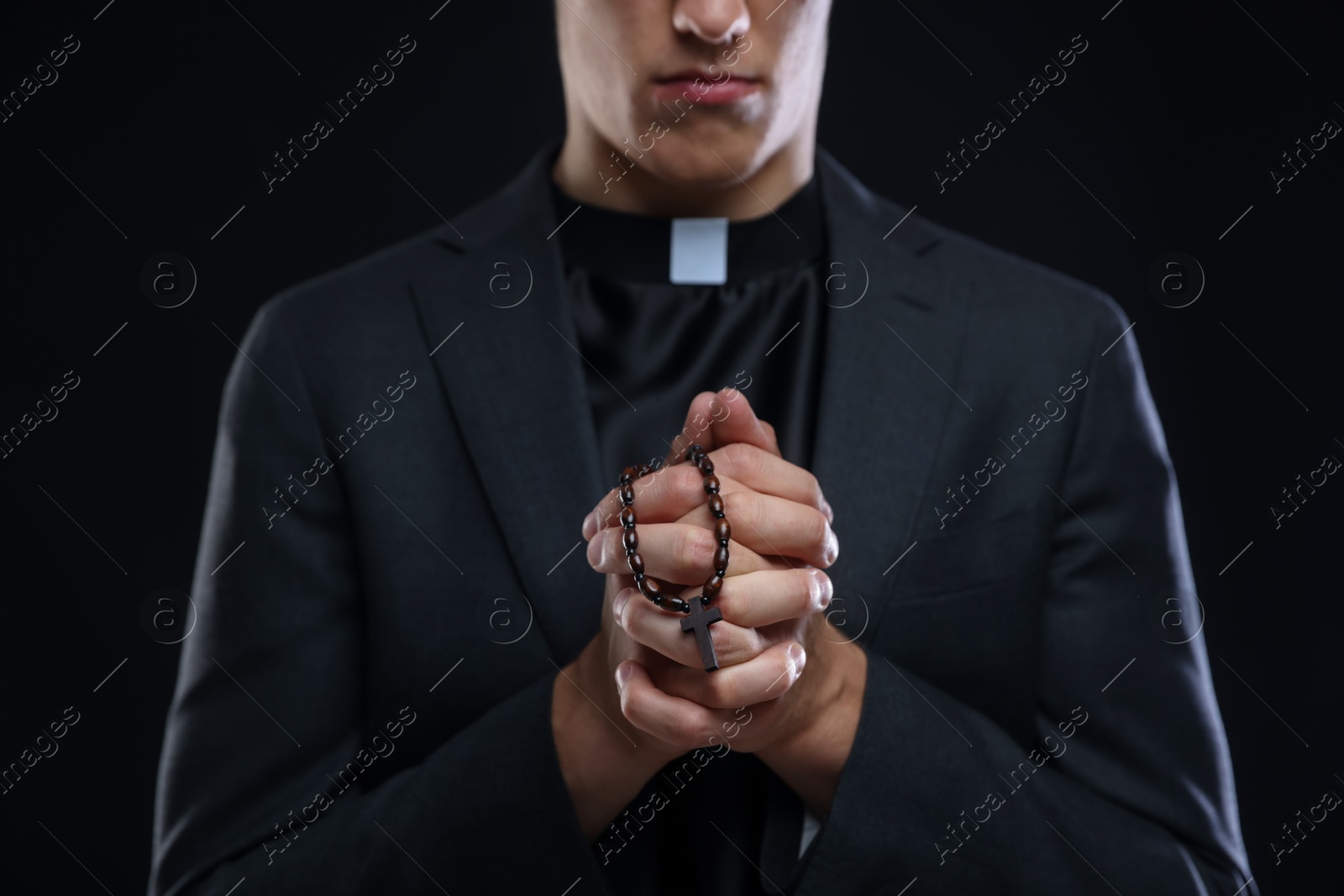 Photo of Priest with rosary praying on black background, closeup