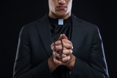 Photo of Priest with rosary praying on black background, closeup
