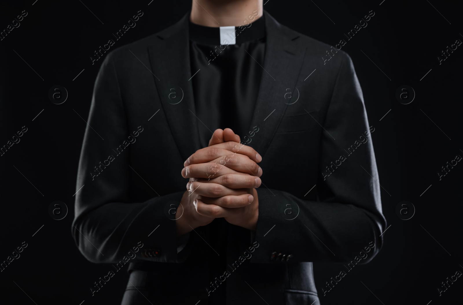 Photo of Priest praying on black background, closeup view