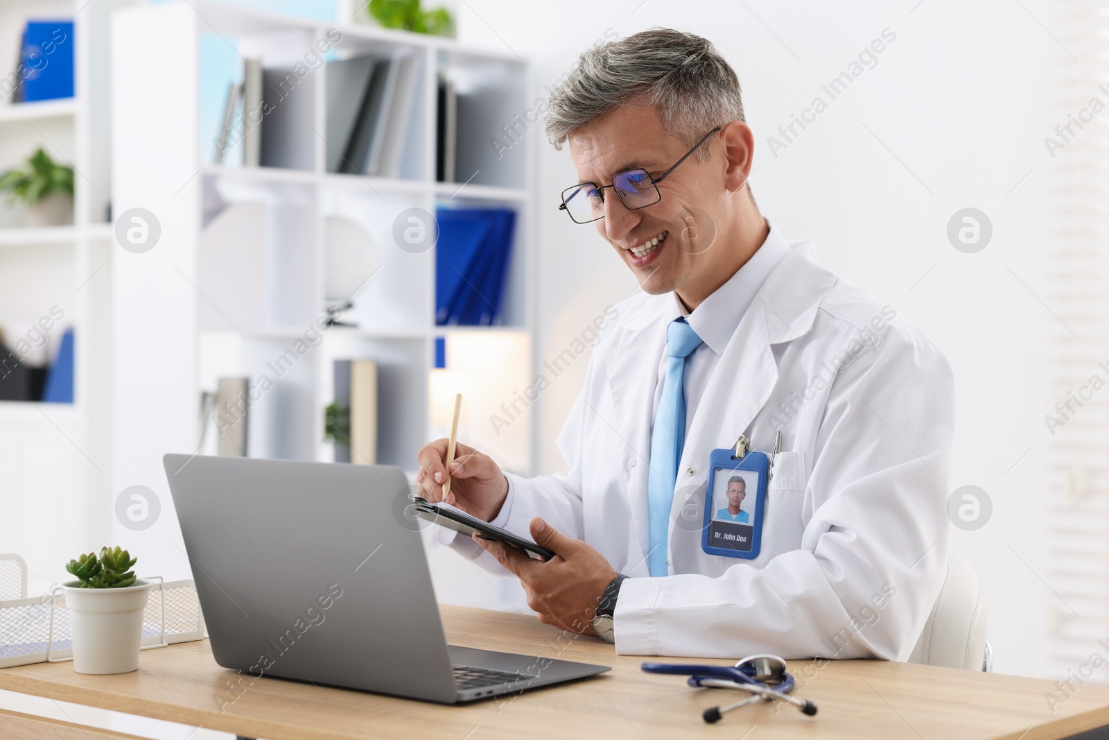 Photo of Telemedicine. Doctor making notes while having video call with patient via laptop indoors