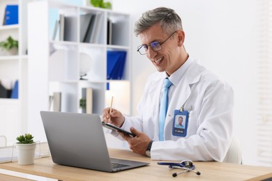 Photo of Telemedicine. Doctor making notes while having video call with patient via laptop indoors