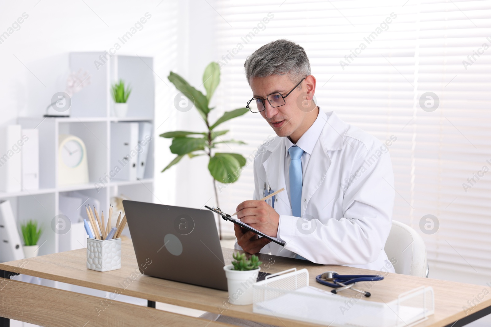 Photo of Telemedicine. Doctor making notes while having video call with patient via laptop indoors