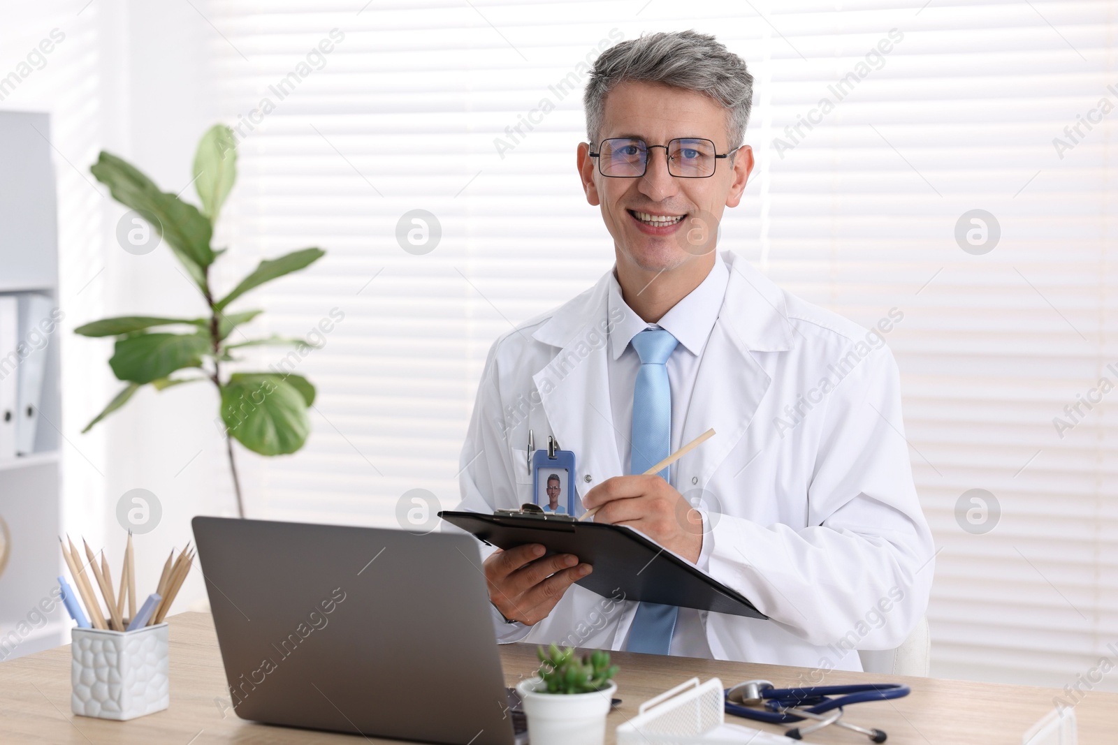 Photo of Telemedicine. Doctor making notes while having video call with patient via laptop indoors