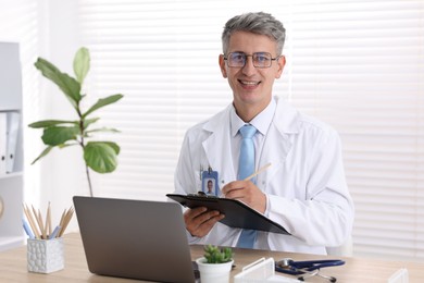 Photo of Telemedicine. Doctor making notes while having video call with patient via laptop indoors