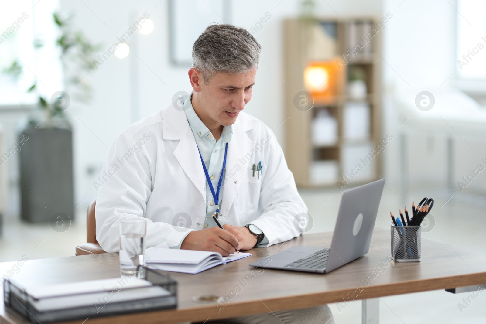 Photo of Telemedicine. Doctor making notes while having video call with patient via laptop indoors