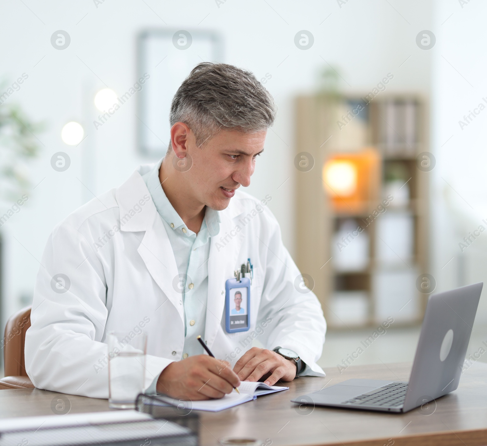 Photo of Telemedicine. Doctor making notes while having video call with patient via laptop indoors
