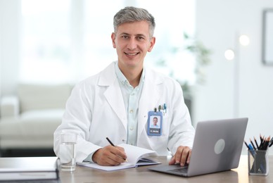 Photo of Telemedicine. Doctor making notes while having video call with patient via laptop indoors