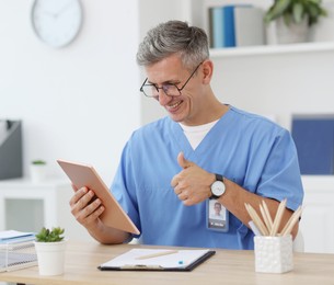 Photo of Telemedicine. Doctor showing thumbs up during video call with patient via tablet indoors