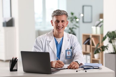 Photo of Telemedicine. Doctor making notes while having video call with patient via laptop indoors
