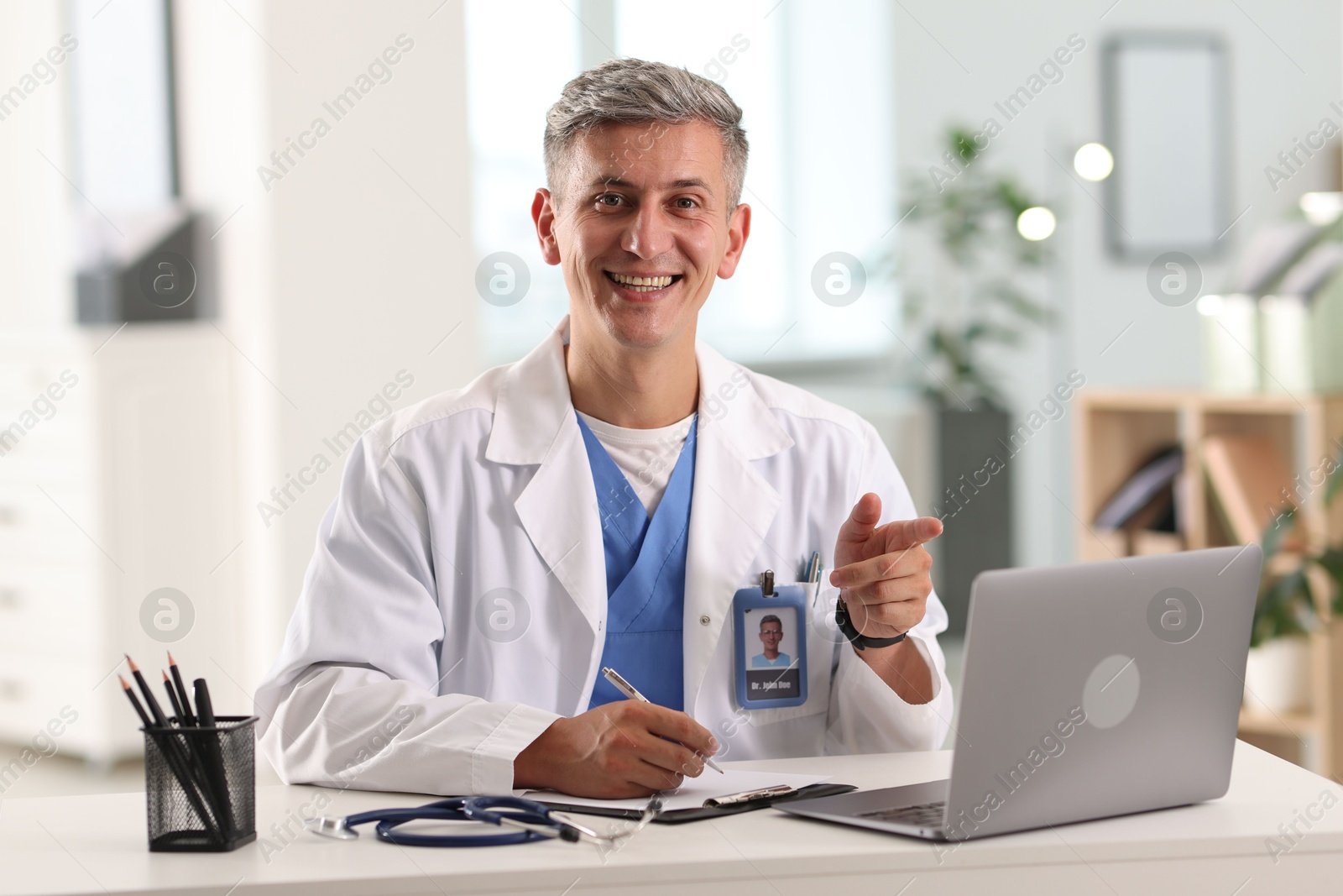 Photo of Telemedicine. Doctor making notes while having video call with patient via laptop indoors