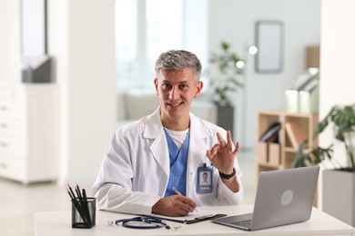 Photo of Telemedicine. Doctor making notes while having video call with patient via laptop indoors