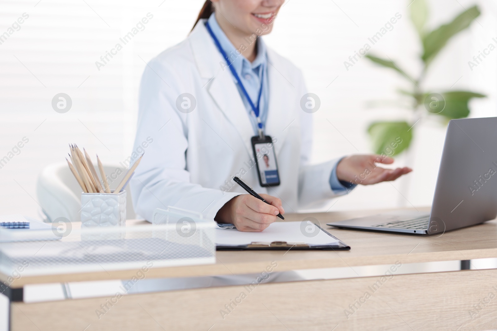 Photo of Telemedicine. Doctor making notes while having video call with patient via laptop indoors, closeup