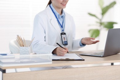Photo of Telemedicine. Doctor making notes while having video call with patient via laptop indoors, closeup