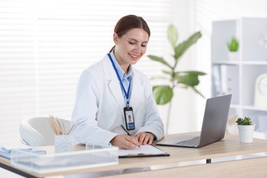 Photo of Telemedicine. Doctor making notes while having video call with patient via laptop indoors