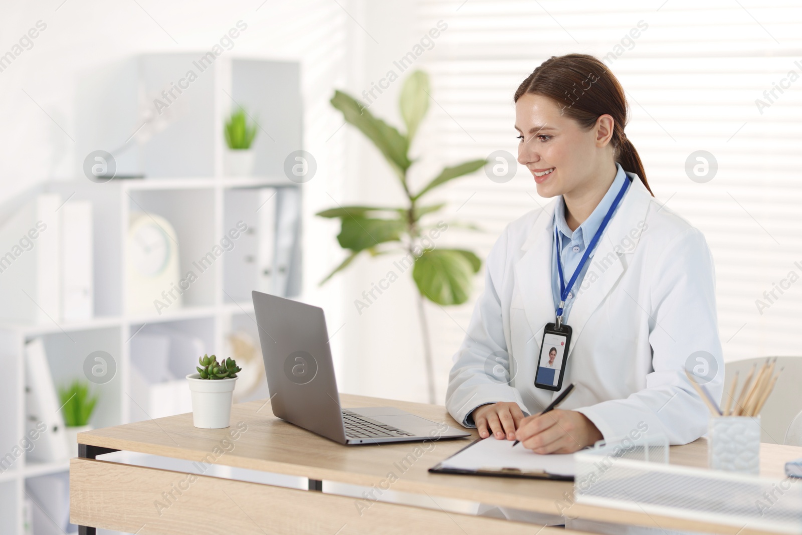 Photo of Telemedicine. Doctor making notes while having video call with patient via laptop indoors