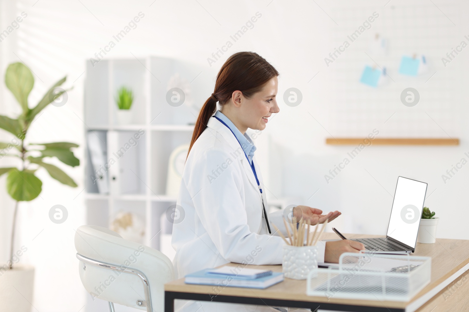 Photo of Telemedicine. Doctor making notes while having video call with patient via laptop indoors