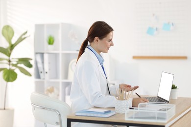 Photo of Telemedicine. Doctor making notes while having video call with patient via laptop indoors