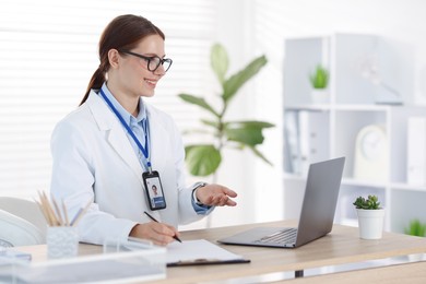 Photo of Telemedicine. Doctor making notes while having video call with patient via laptop indoors