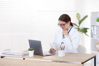 Photo of Telemedicine. Doctor making notes while having video call with patient via laptop indoors