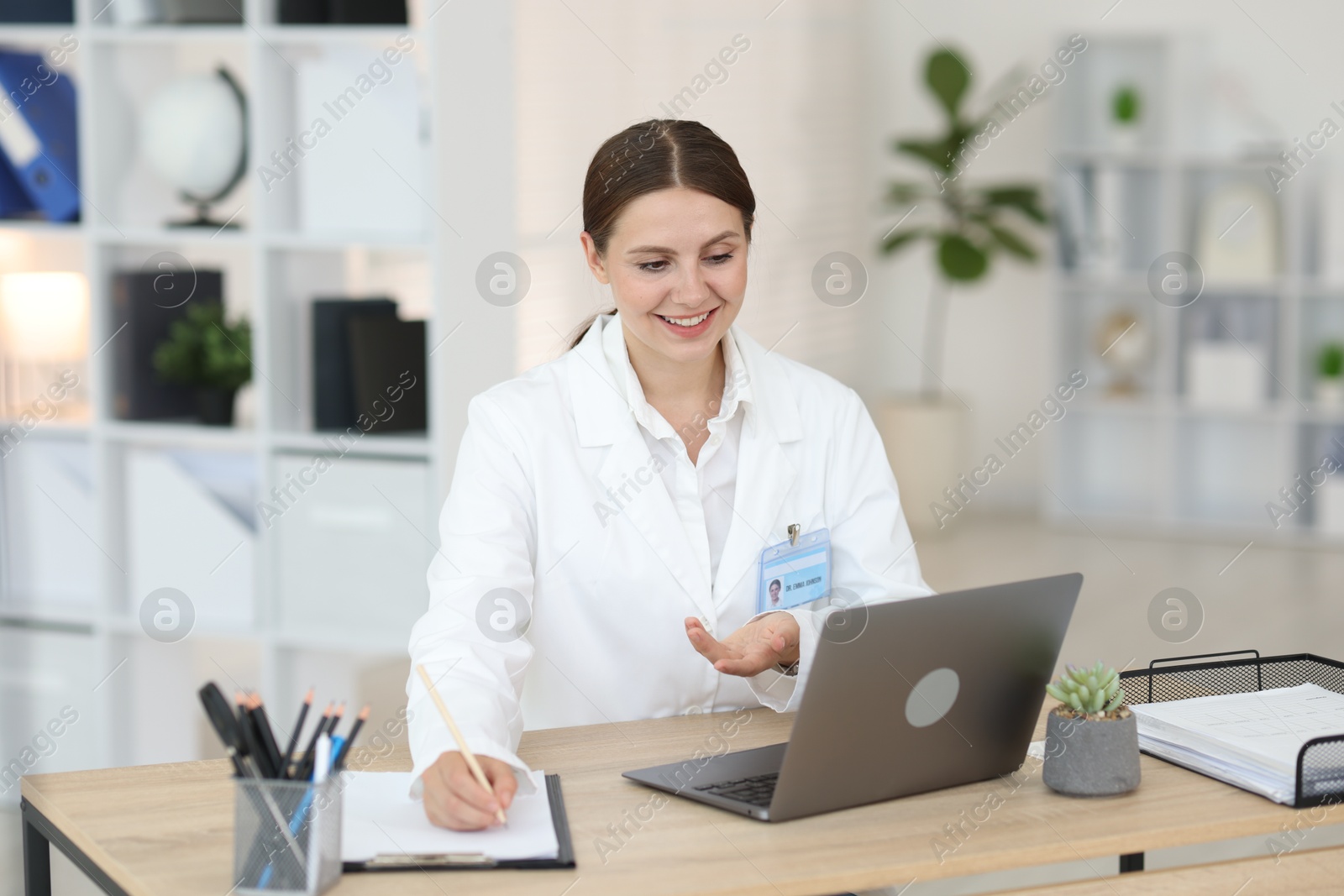 Photo of Telemedicine. Doctor making notes while having video call with patient via laptop indoors