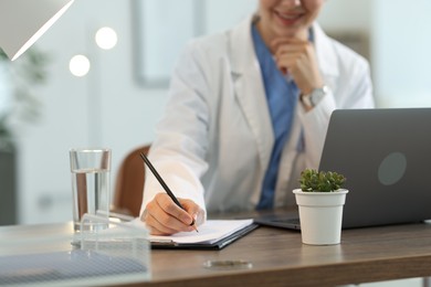Photo of Telemedicine. Doctor making notes while having video call with patient via laptop indoors, closeup