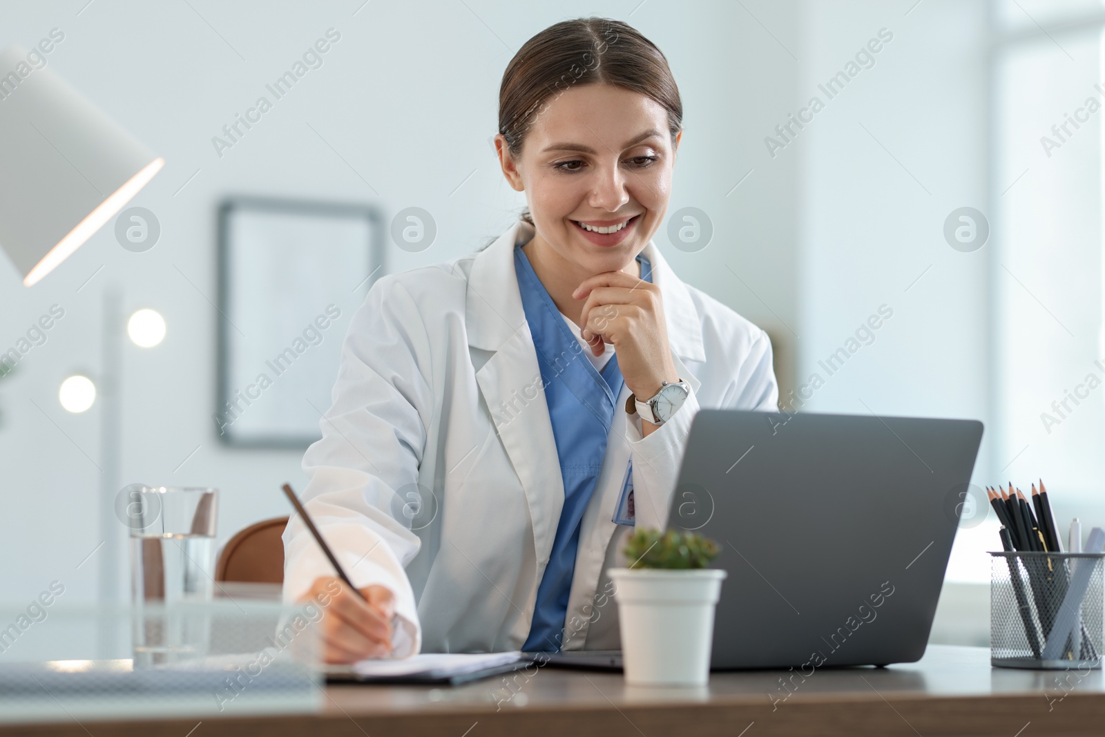 Photo of Telemedicine. Doctor making notes while having video call with patient via laptop indoors